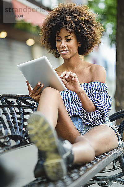 Portrait of young woman with curly hair sitting on bench using tablet