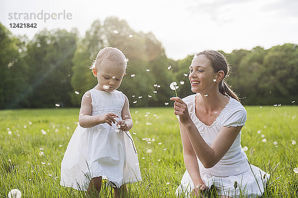 Mother and daughter with blowballs on meadow in summer