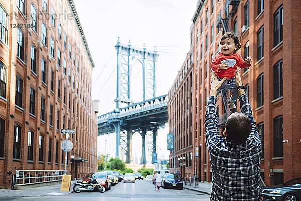 USA  New York  New York City  Father playing with baby in Brooklyn with Manhattan Bridge in the background