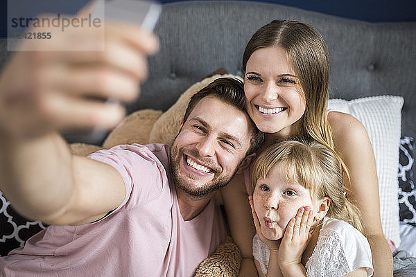 Happy family sitting on bed  taking smartphone selfies