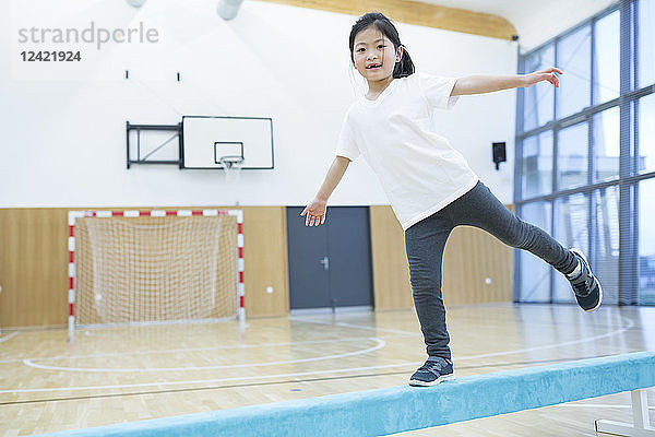 Schoolgirl balancing on balance beam in gym class