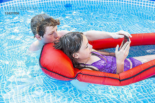 Brother and sister in swimming pool looking at smartphone