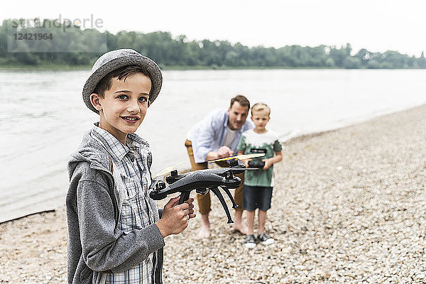 Portrait of smiling boy with father and brother playing with drone at the riverside