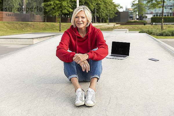 Senior woman wearing red hoodie sitting outdoors with laptop