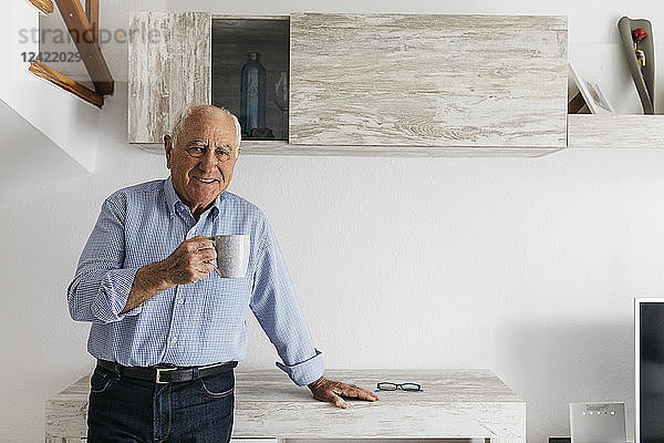 Senior man having a coffee while relaxing at home  looking at camera