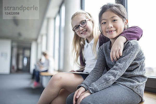 Portrait of two smiling schoolgirls sitting on school corridor