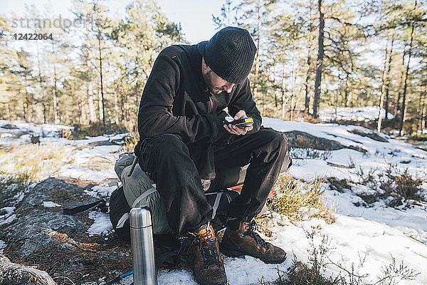 Sweden  Sodermanland  backpacker resting in remote landscape in winter using GPS tracker