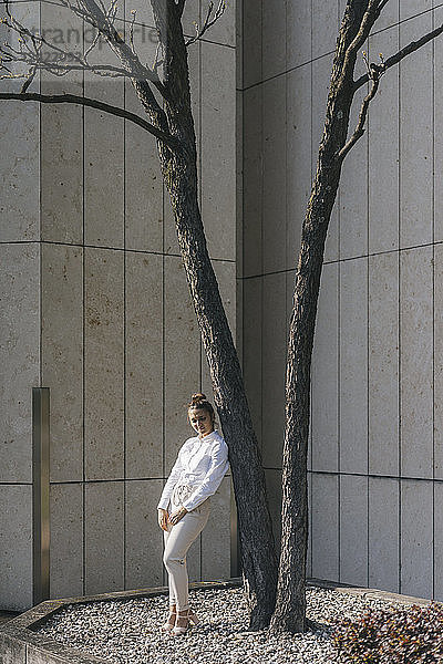 Young businesswoman leaning against atree in a backyard