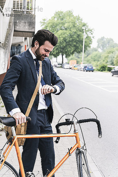 Smiling businessman with bicycle at the street checking the time