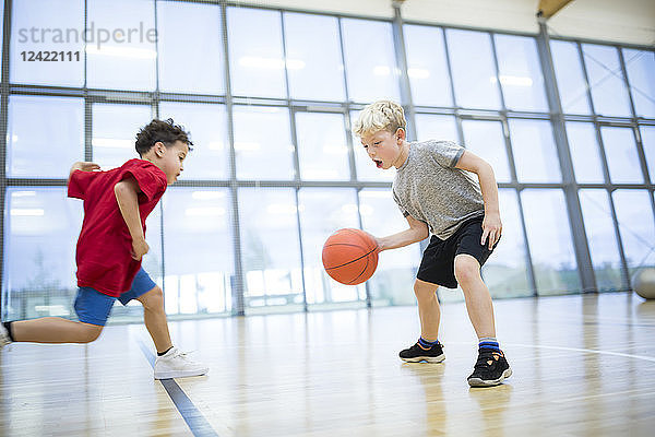 Two schoolboys playing basketball in gym class