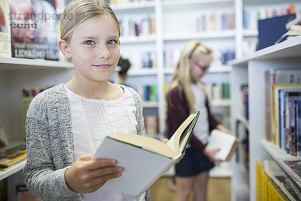Portrait of smiling schoolgirl with book in school library