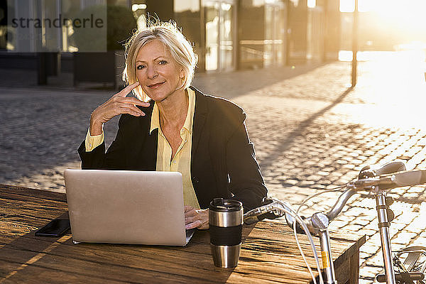 Smiling senior businesswoman using laptop in the city at sunset