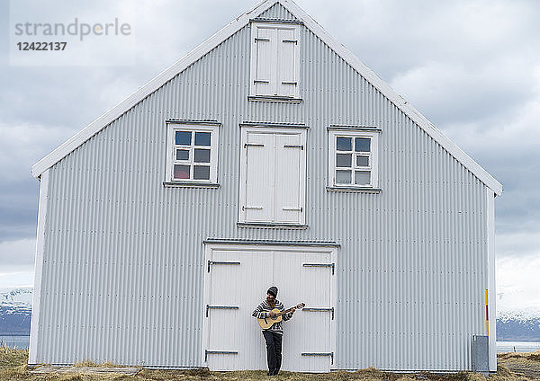 Iceland  young man playing guitar  wooden house