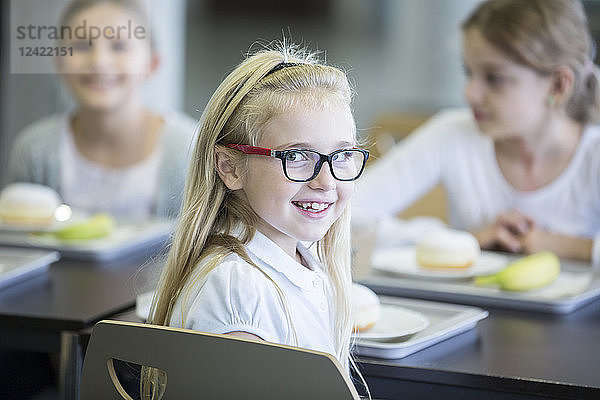 Portrait of smiling schoolgirl with classmates in school canteen