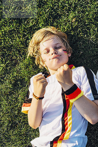 Boy in German soccer shirt lying on grass  keeping fingers crossed for world chamiponship