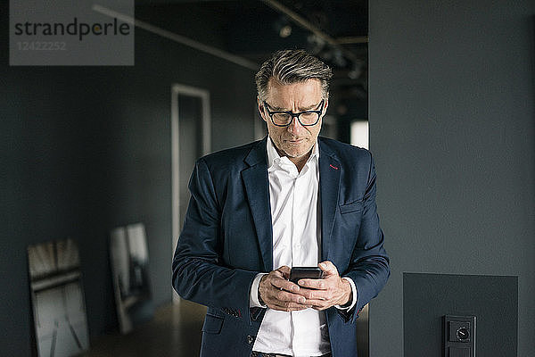 Mature businessman standing in office using cell phone