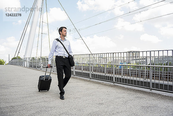 Businessman in the city with rolling suitcase crossing a bridge