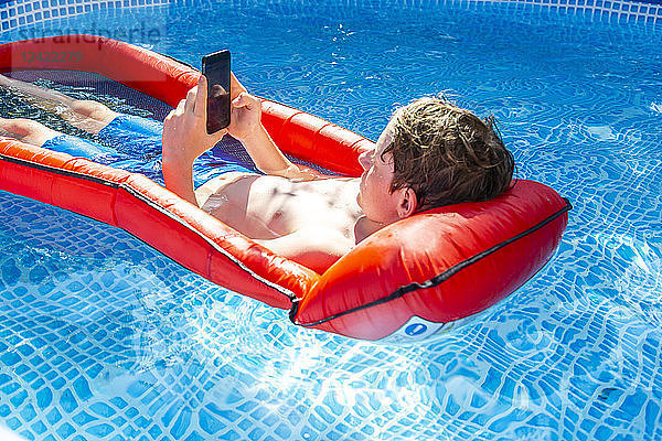 Boy floating on water in swimming pool using smartphone