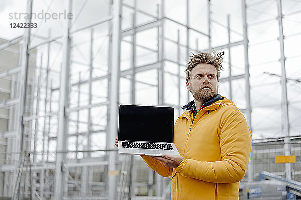 Man holding laptop  construction site in the background