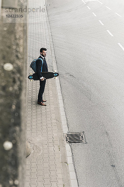 Businessman carrying skateboard standing at the street