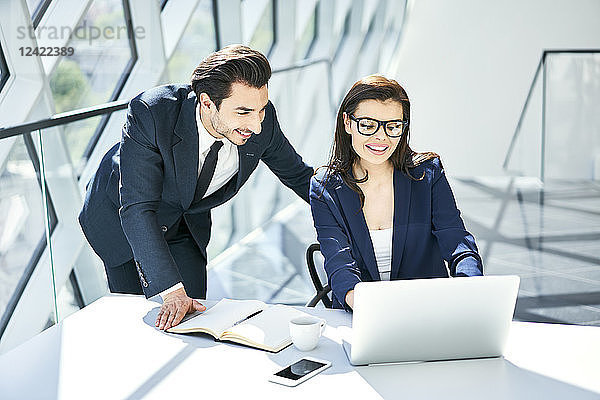 Smiling businesswoman and businessman using laptop at desk in modern office