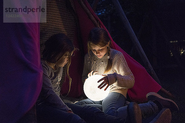 Two girls sitting in tipi  holding lamp as moon