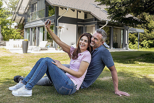 Happy couple sitting in garden of their home taking a selfie