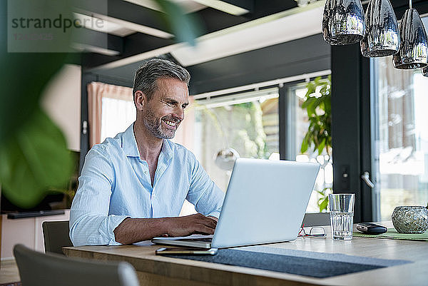 Smiling mature man at home using a laptop at table