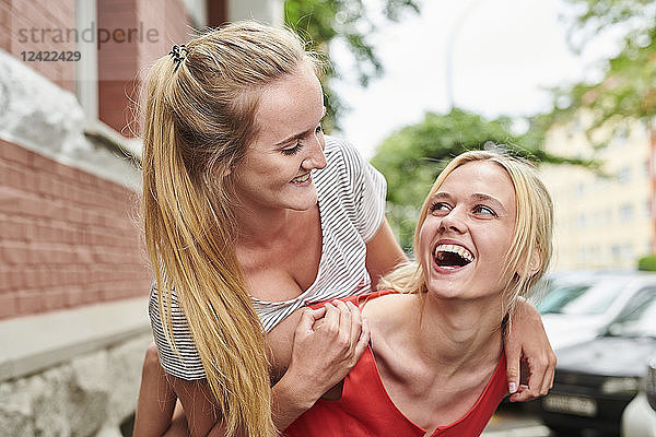 Happy young woman giving friend piggyback ride in the city