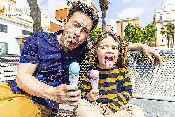 Spain  Barcelona  happy father and son sitting on bench enjoying an ice cream