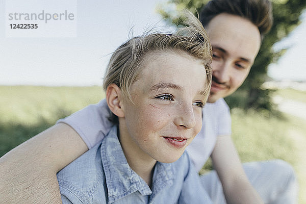 Portrait of young man embracing smiling boy at a field
