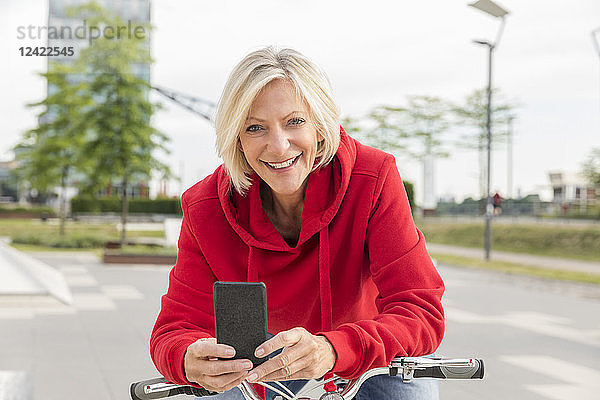 Portrait of smiling senior woman with city bike and cell phone