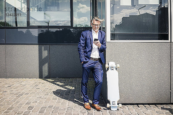 Mature businessman using cell phone outdoors next to longboard