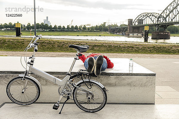 Senior woman with city bike having a break lying on platform