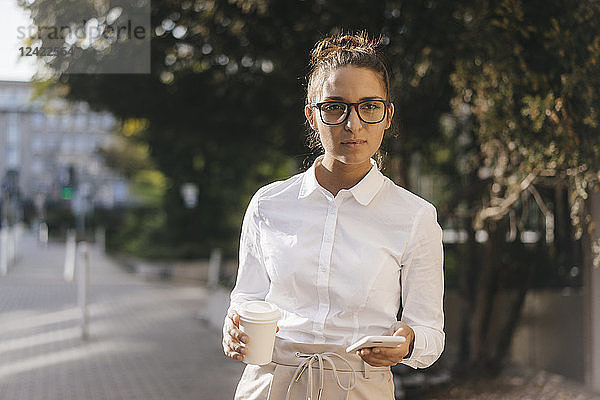 Young businesswoman carrying cup of coffee and a smartphone