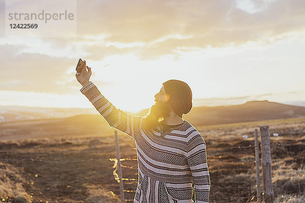 Iceland  young man using smartphone  selfie at sunset