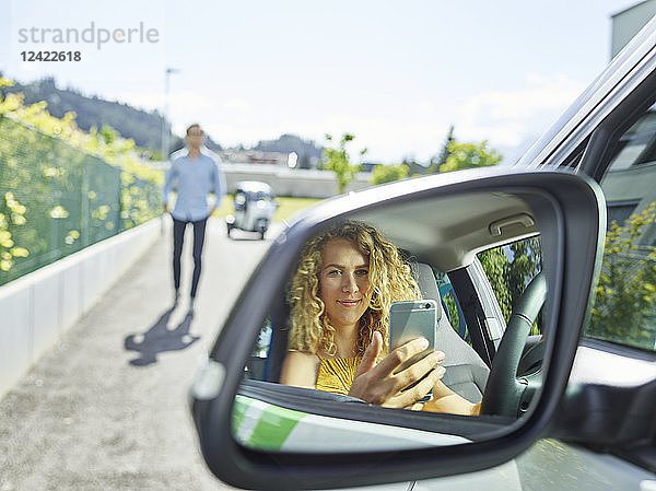 Smiling young woman using cell phone in electric car