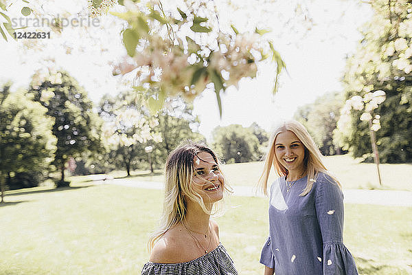 Two happy young women in a park at blossoming tree