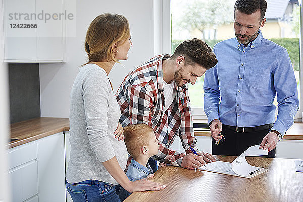 Family with real estate agent signing contract in kitchen of new apartment