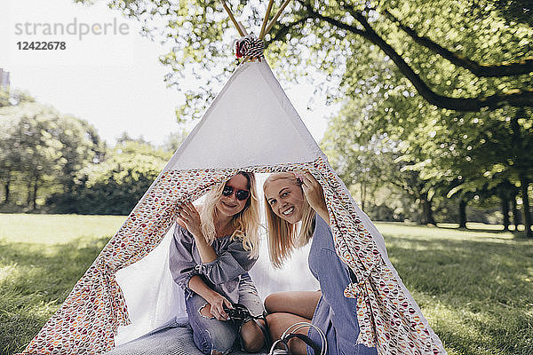 Two happy young women with old-fashioned camera in a teepee in a park