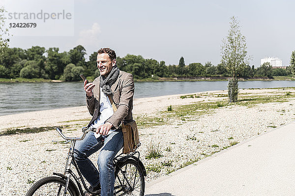 Mature man with bike using smartphone at Rhine riverbank