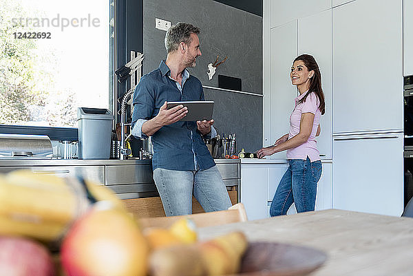 Couple in kitchen at home cooking and using a tablet