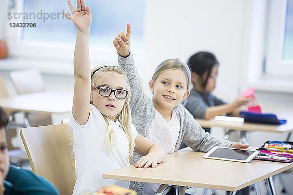 Schoolgirls with tablet raising their hands in class