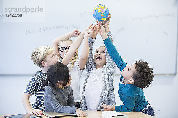 Happy pupils holding globe together in class