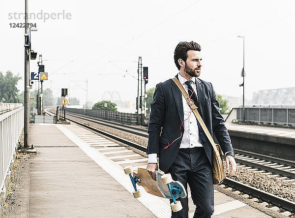 Businessman with skateboard and earphones walking at the platform