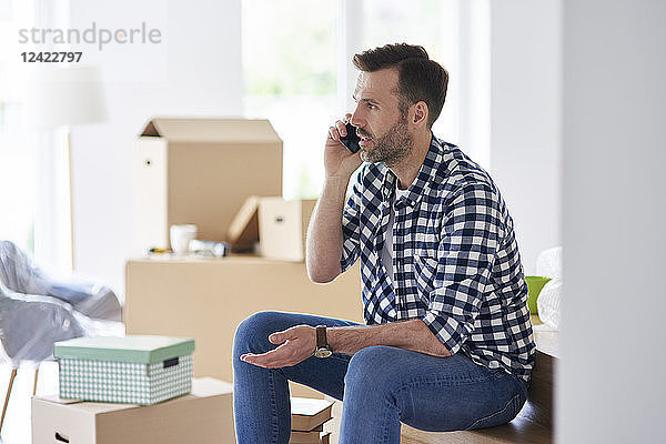 Serious man moving into new flat talking on cell phone