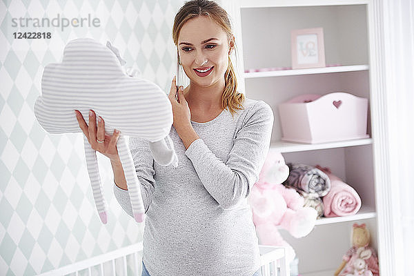 Pregnant woman with cushion and smartphone in baby room