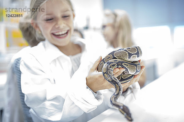 Happy schoolgirl in science class holding snake