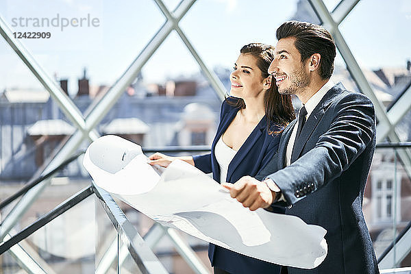 Smiling businesswoman and businessman holding plan in office