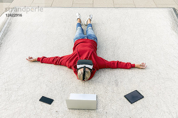 Senior woman lying on the ground wearing VR glasses next to mobile devices